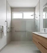 A level-entry shower with no hob, grab rails on two walls, a glass screen and a wall-hung vanity
