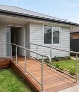 A timber-decked access ramp with stainless steel handrails on both sides, leading to the front door of a single-storey home