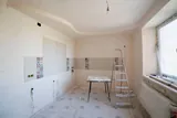 A room part-way through renovation, with fresh plaster, partly tiled walls, roughed-in power outlets and a stepladder